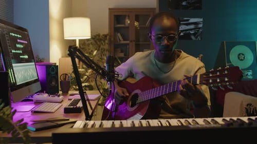Musician Using Computer and Playing Guitar in Home Studio
