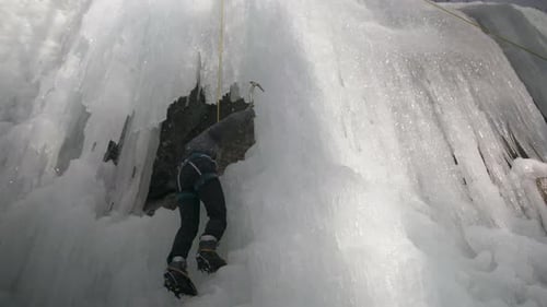 Climber uses ice picks to climb onto a ledge , located on a large ice wall.
