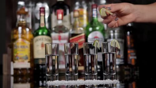 Closeup of a Bartender Putting Lime Slices on a Shot Glass with Tequila