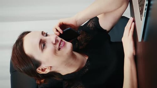 Portrait of young businesswoman talking on smartphone in front of laptop computer in modern office