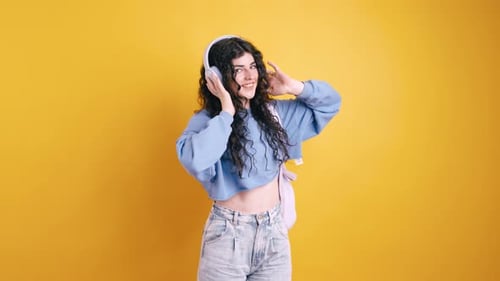 Energetic Woman Dancing with Headphones on Yellow Backdrop