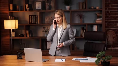 Focused Smiling Business Woman Talking on Mobile Phone Using Laptop in Office