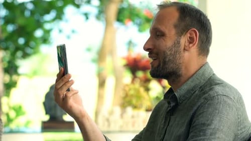 Young, Happy Man Chatting on Smartphone and Drinking Beverage in Garden 30s