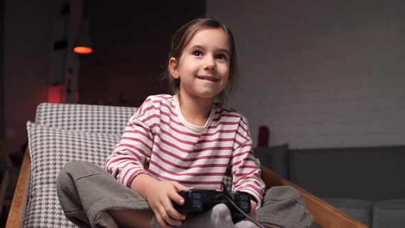 Niña jugando videojuegos sentada en un sillón en casa, Grabaciones de ...