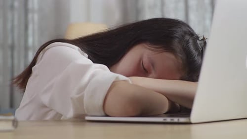 Bored Asian Teenager Yawning And Sleep At Home While Doing Home Work On Laptop Computer