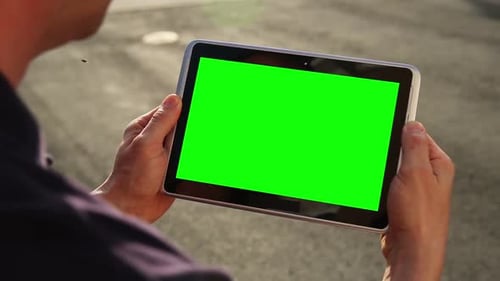 Synergy Collection: Over the shoulder view of a tablet in a man's hand with a green screen element