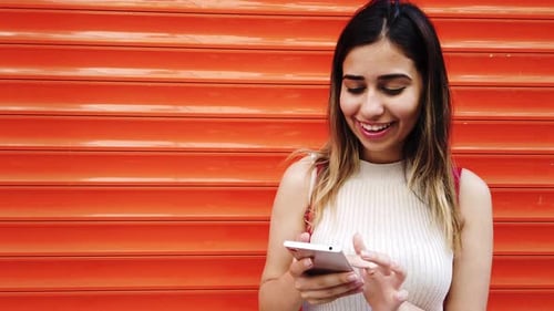Happy Woman Uses Mobile Phone Against Orange Wall