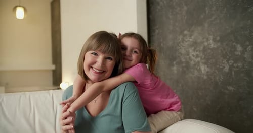 Child Hugging Grandmother Smiling on White Couch