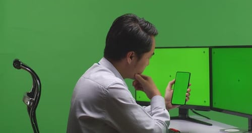 Asian Man Using Mobile Phone And Multiple Computer Monitor With Mock Up Green Screen In Green Screen