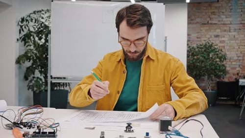 Un homme concentré à lunettes corrige le schéma du prototype de l'appareil