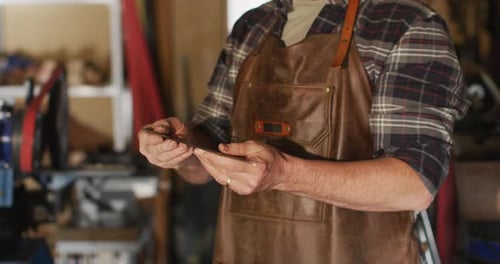 Midsection of caucasian male knife maker in workshop, holding knife