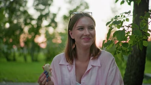 Woman Enjoys Sandwich Outdoors in City Park at Sunset