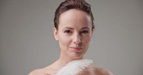 Woman Touching Face with White Feather in Studio
