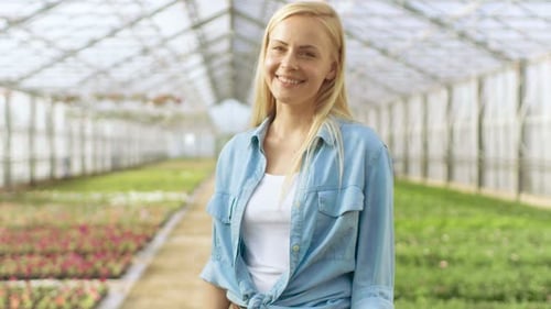 Smiling Woman in Greenhouse with Flower Rows