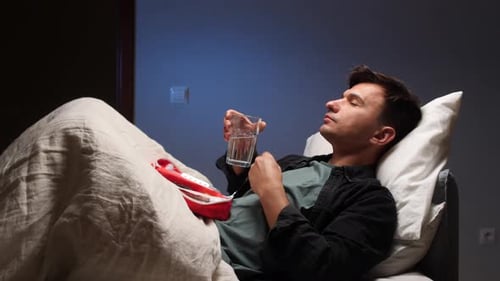Man Lying in Bed Taking Pill with Water