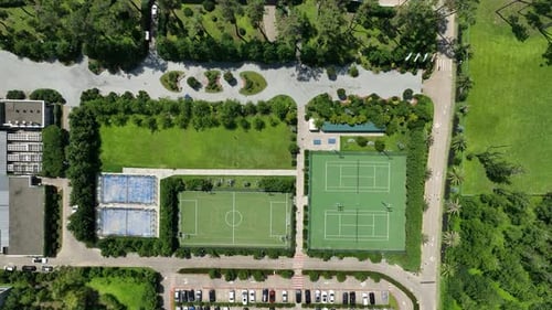 Aerial View Of Green Tennis Courts With Lights, Nets, And Fenced Boundaries Overlooking Parks Nearby
