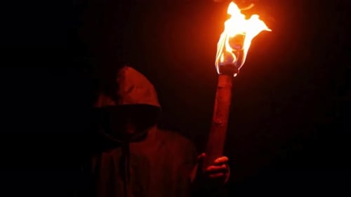 Hooded Figure Holding a Burning Torch at Night