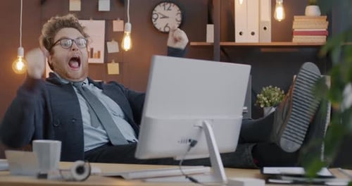 Loop of Excited Employee Screaming and Gesturing Expressing Joy Sitting at Computer Desk in Evening