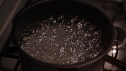 Nahaufnahme von klarem Wasser, das in einem schwarzen Topf auf dem Herd kräftig kocht und zahlreiche kleine Blasen erzeugt