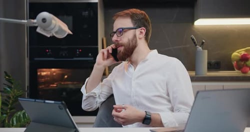 Man Talking on Phone with Laptops in Kitchen