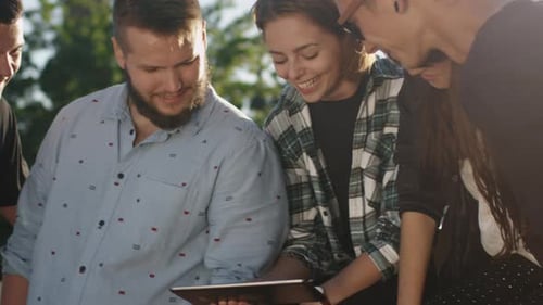 Friends Looking at Tablet Outdoors in Sunlight