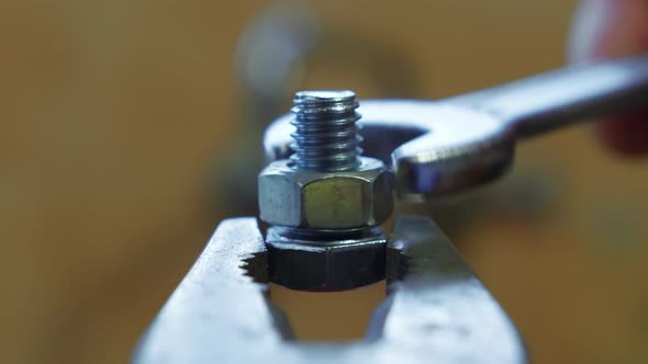 Clockwise of a wrench turning a bolt on a screw held by pliers, close ...