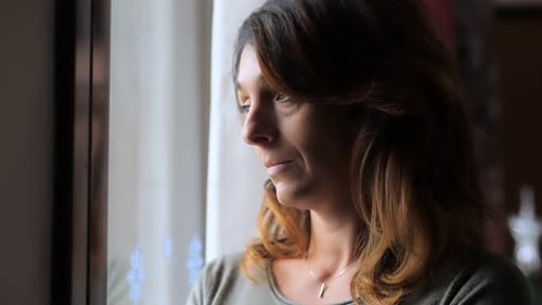 Sad pensive beautiful young lonely woman looking out the window