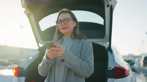 Woman Using Smartphone Near Car on a Sunny Day