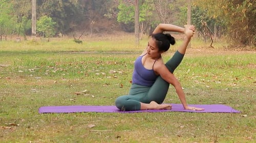 Asian woman practicing yoga on mat in outdoor park.