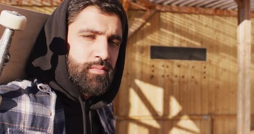Video of midsection of middle eastern male skateboarder holding skateboard in skate park