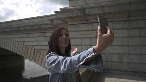 Brunette Latina tourist using Skype and showing her friend the river Thames and Putney Bridge in Lon