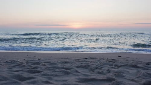 Slow-motion video of gentle sea waves rolling onto the sandy beach at sunset.