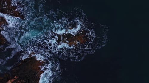 Waves crash on rocks during the day near the ocean shoreline