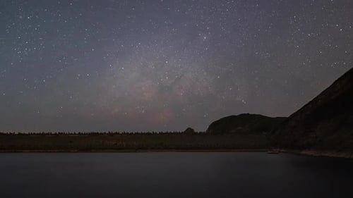 Shining stars at dark night over silhouette of trees and mountains reflecting on calm sea surface in