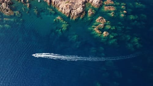 Aerial shot of a boat sailing in the blue sea near rocky coastal cliffs on a sunny summer day.