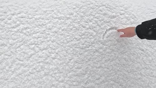 Hand Draws Heart Shape in Fresh White Snow