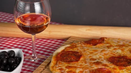 Freshly Baked Pepperoni Pizza On A Wooden Board With Rose Wine On The Side And Black Olives