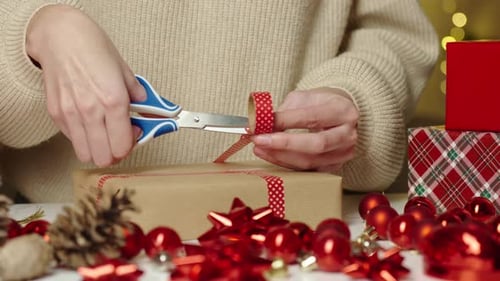 Woman Wrapping Christmas Present With Red Ribbon