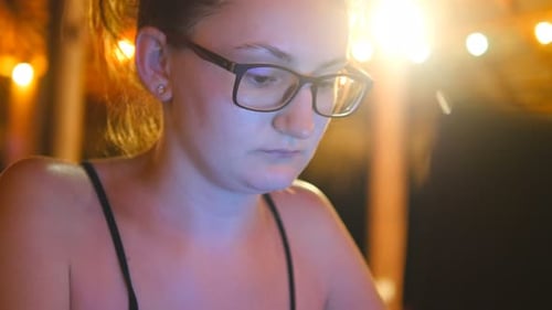 Young Woman Uses Laptop at Outdoor Cafe at Night