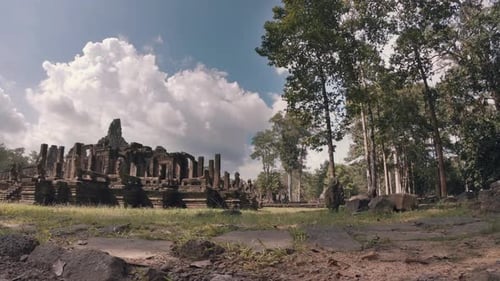 Zeitraffer des Tempels im Angkor Wat Komplex zwischen Bäumen mit flauschigen weißen Wolken