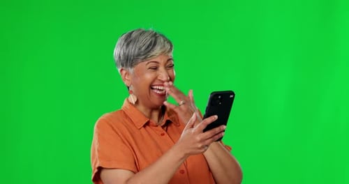 Senior woman, phone and laughing on green screen for funny meme, joke or social media against studio