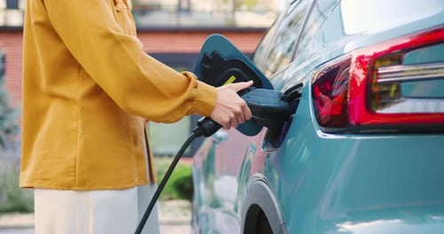 Nahaufnahme weiblicher Hände, die ein Elektroauto-Ladegerät an ihr Fahrzeug im Freien anschließen