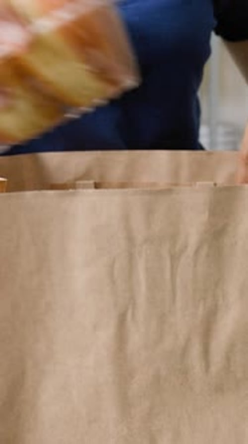 Vertical of Female Employee Packing Food in Takeaway Paper Bag at Dark Store