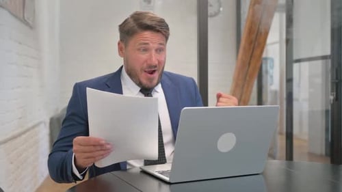 Excited Businessman Working at Laptop in Office Setting
