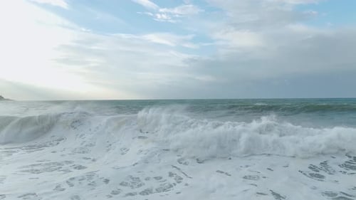 Aerial Video Towering Waves Crash Ashore Leaving Intricate Foam Designs Across the Scenic Beach