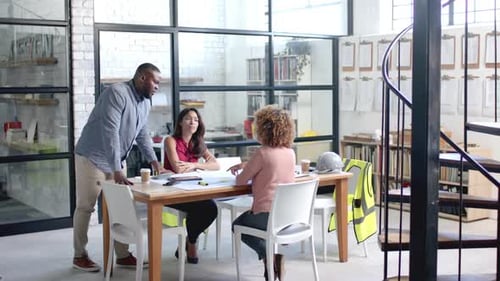 Diverse male and female architects having meeting and looking at blueprints at office, slow motion