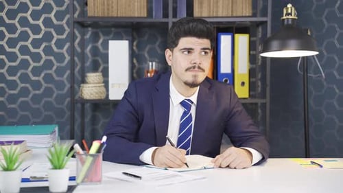 Young Man Writing in Notebook at Office Desk