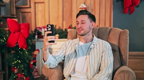 Man Relaxing in Chair Using Phone for Video Call