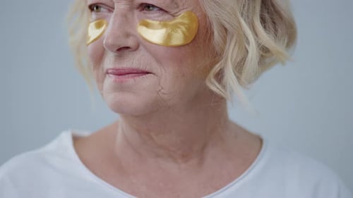 Senior Woman Applying Golden Eye Patches in Home