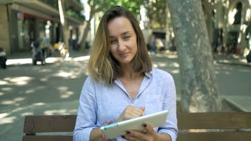 Smiling businesswoman with tablet enjoying city park bench on a sunny day